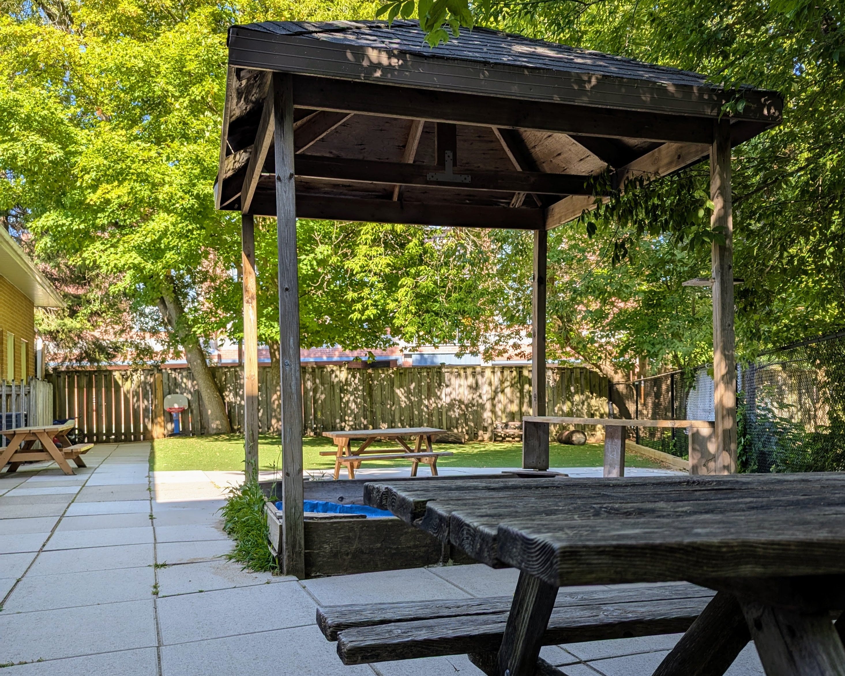 Wooden picnic table with a canopy in a large fenced yard shaded by large trees
